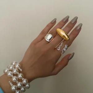 Gold and silver mixed metal statement rings on female hand with grey press-on nails and pearl bracelet - close-up styling shot
