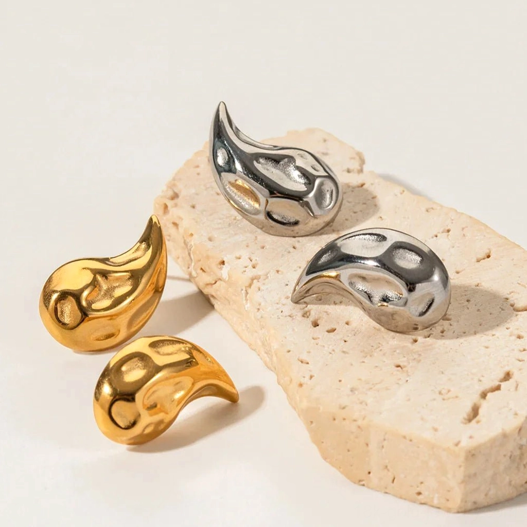 Mixed metal teardrop stud earrings collection featuring 18K gold and silver tones, angled flat lay view on stone background showing textured finish detail