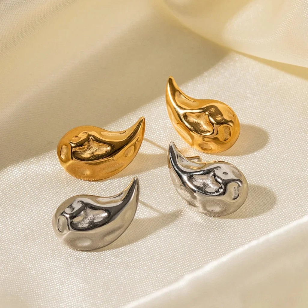 Polished 18K gold and silver teardrop stud earrings set on luxury satin fabric, angled flat lay showing refined finish and vintage aesthetic
