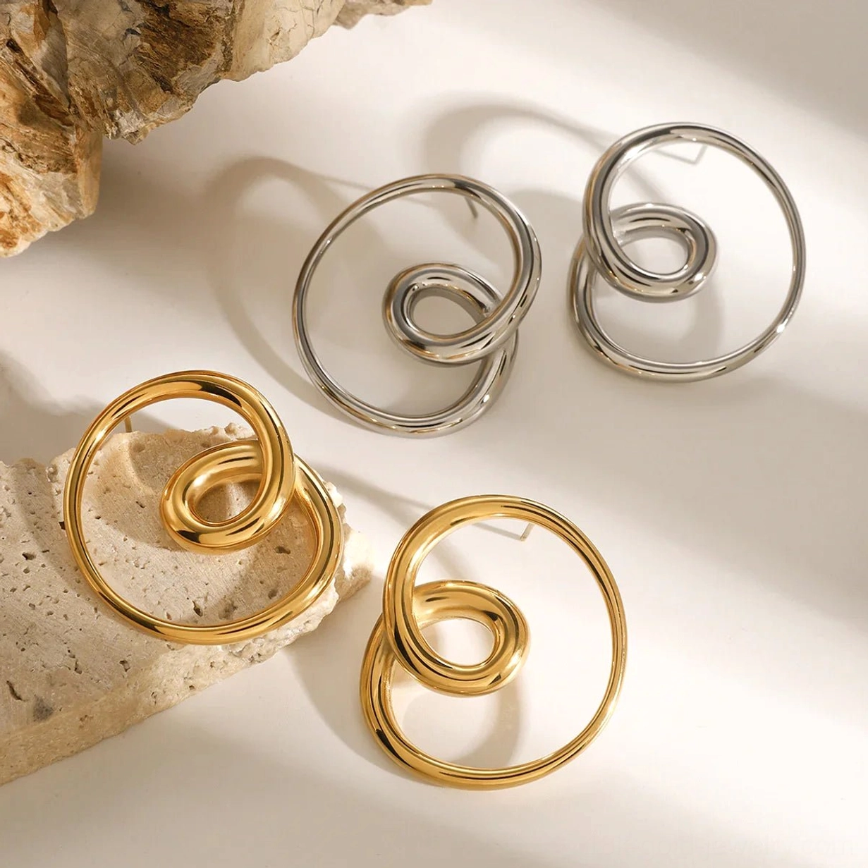Mixed gold and silver spiral stud earrings flat lay rustic stone background comparison