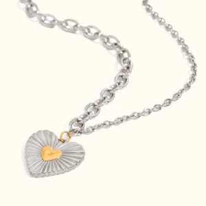 Two-tone heart pendant necklace with 18K gold and silver plating shown on white background, flat lay overhead view showcasing ribbed silver heart with gold center and delicate cable chain
