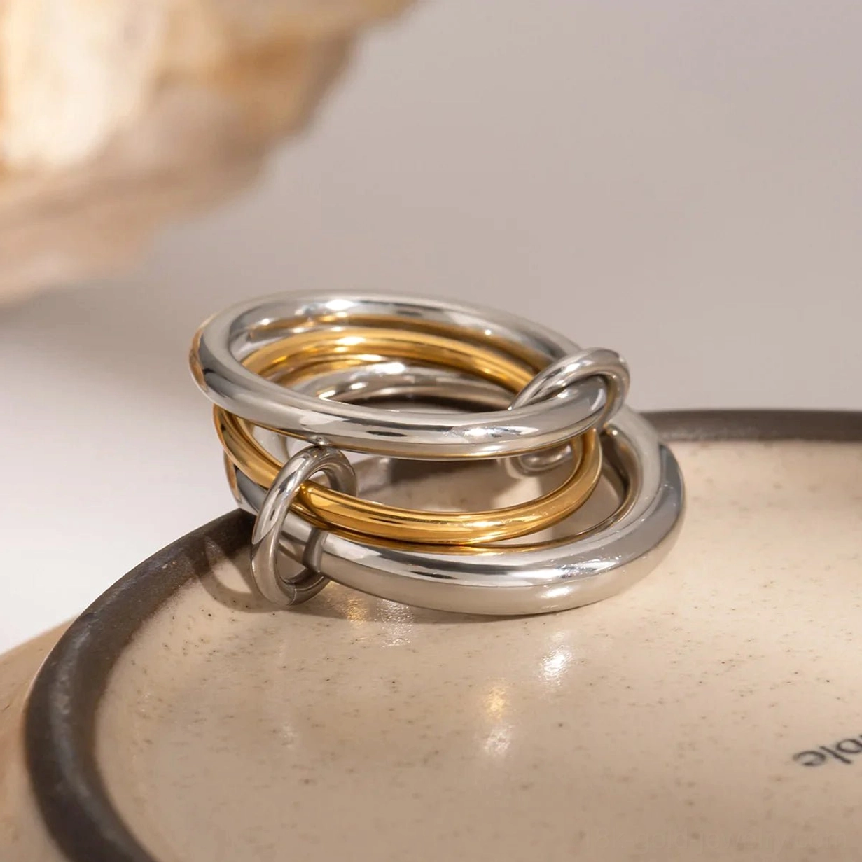 Side view close-up of two-tone stacked rings - 18K gold and silver linked bands on ceramic surface