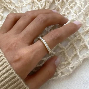 Slim pavé diamond stackable ring close-up top view on hand wearing cream knitwear over crocheted fabric background showing thin band with complete circle of sparkling stones