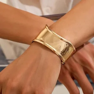18K gold cuff bracelet worn on male wrist close-up, demonstrating snug fit and highly reflective polished gold surface with white shirt backdrop