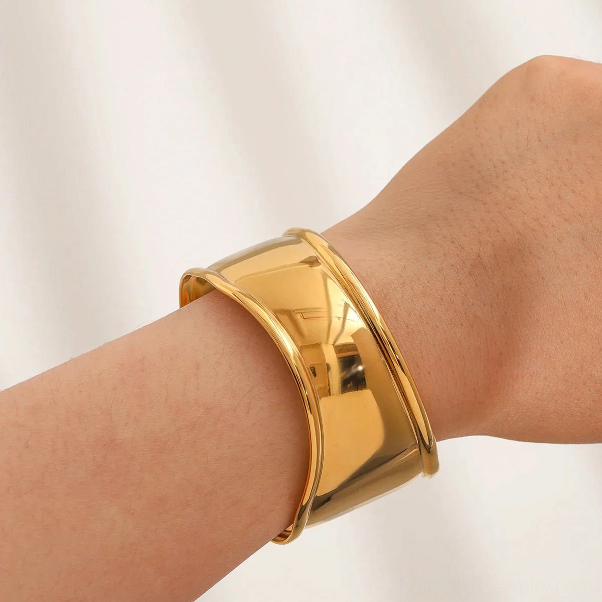 18K gold open cuff bracelet on female forearm, showing curved elegant silhouette and sleek solid gold tone from side perspective