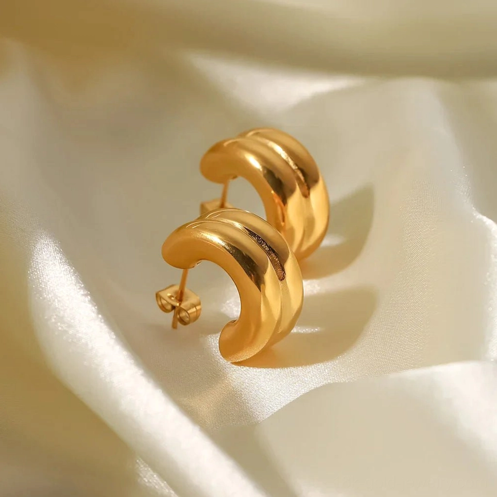 Solid 18K gold double-layer chunky hoop earrings with shiny polished surface, oblique flat lay on ivory satin