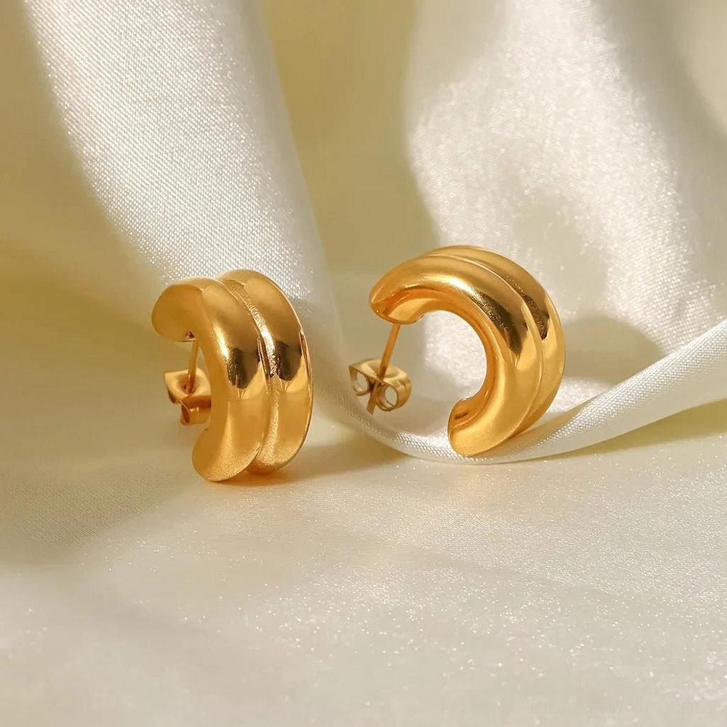 Solid 18K gold double-layer chunky hoop earrings with smooth mirror finish, flat lay side view on ivory satin