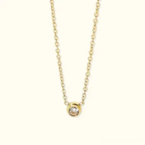 18K gold solitaire necklace with bezel-set CZ diamond pendant, flat lay on neutral background showing delicate chain and brilliant stone detail