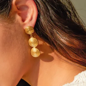 Triple spiral gold earrings worn on model ear close-up side view showing fit and dangling design with wavy brown hair