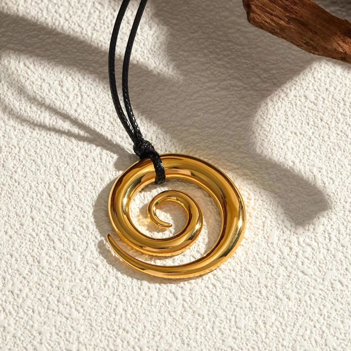 Spiral pendant necklace with double black cords on textured wall with wooden home decor - lifestyle styling angle