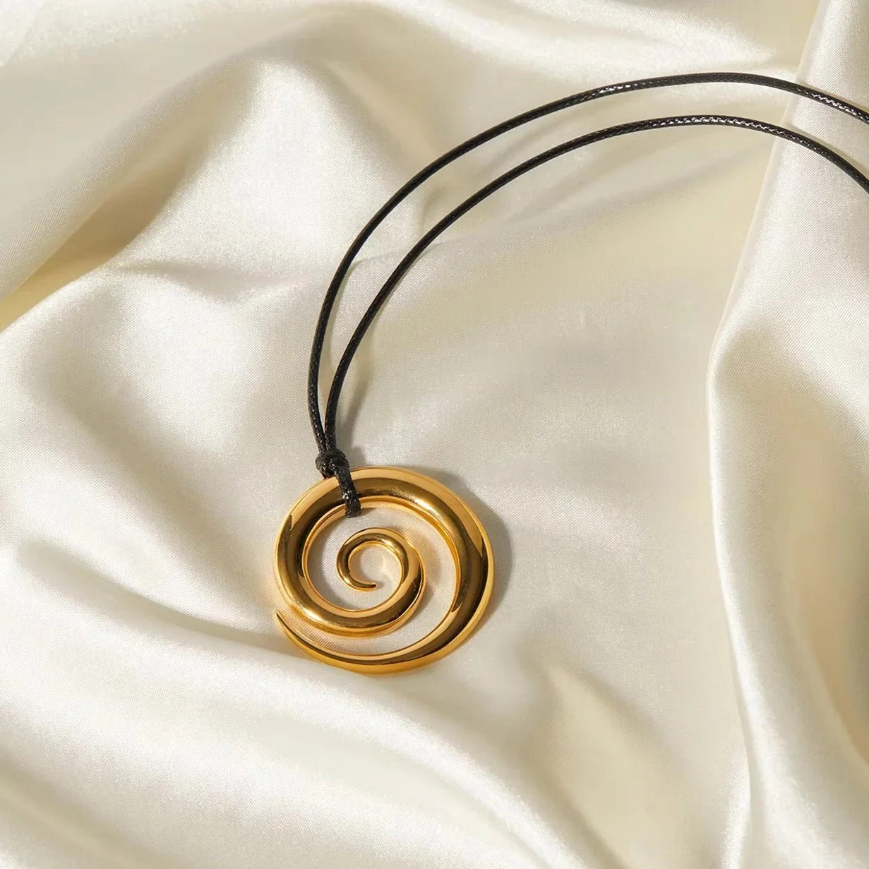 Polished gold spiral charm pendant necklace on satin fabric background - side profile product view