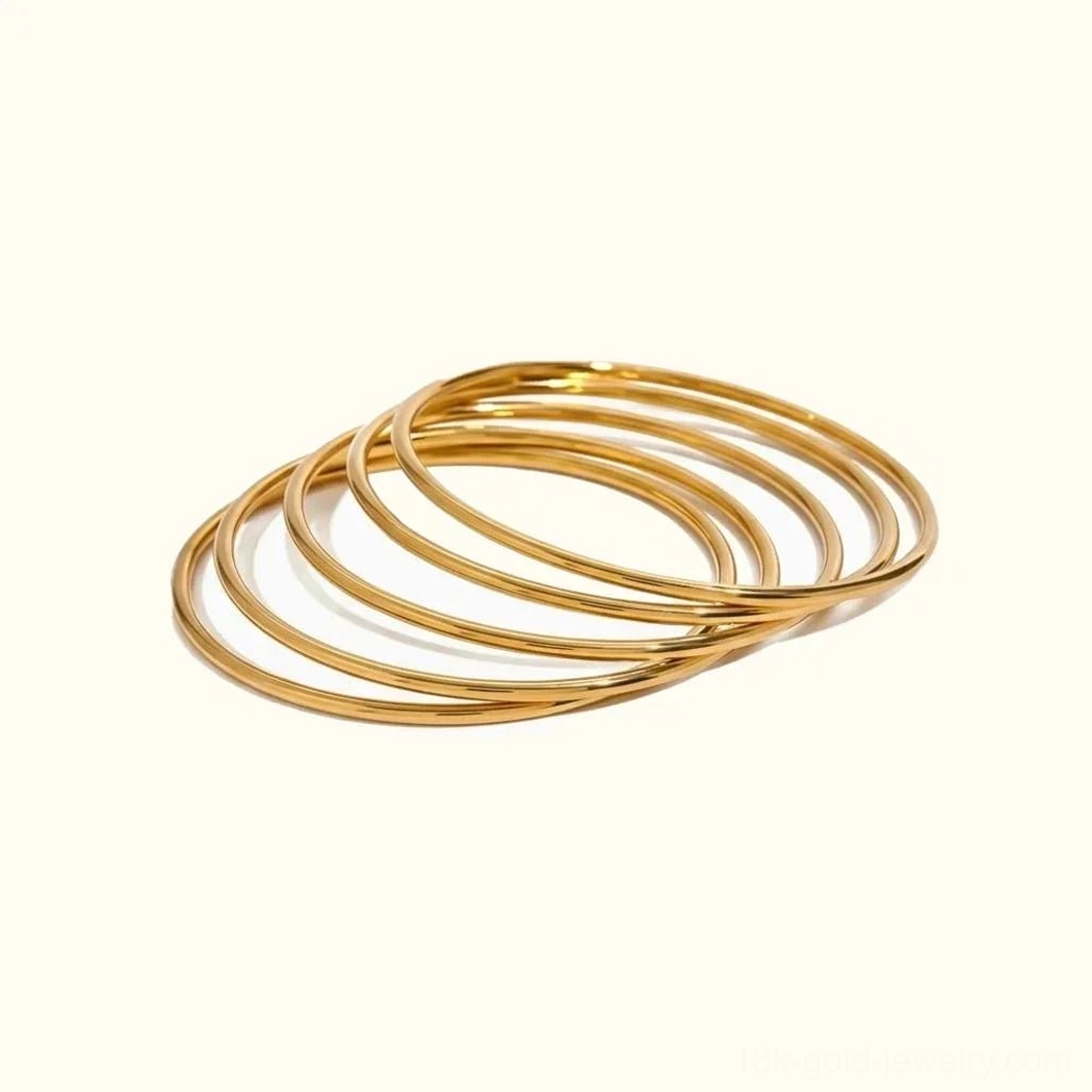 18K gold stackable bangle set flat lay - polished round bangles on neutral background