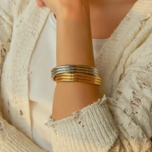 Woman wearing gold stacked open cuff bracelet on wrist, styled with knit cardigan, close-up lifestyle shot