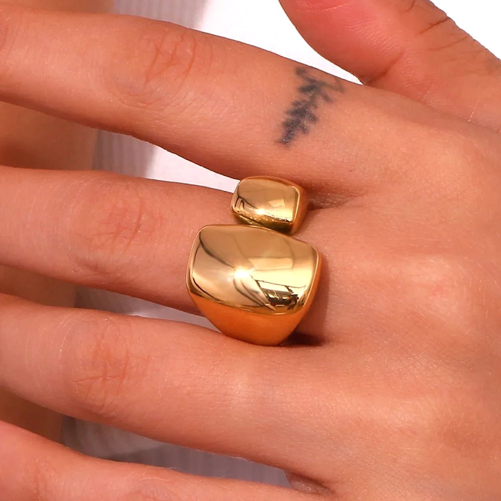 Stacked 18K Gold chunky geometric rings on tattooed female hand, close-up finger view displaying warm golden tone and polished glossy surface