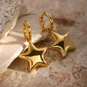 Close-up angled side view of 18K gold star earrings on natural stone slab background displaying high-shine gold finish and solid star charm details