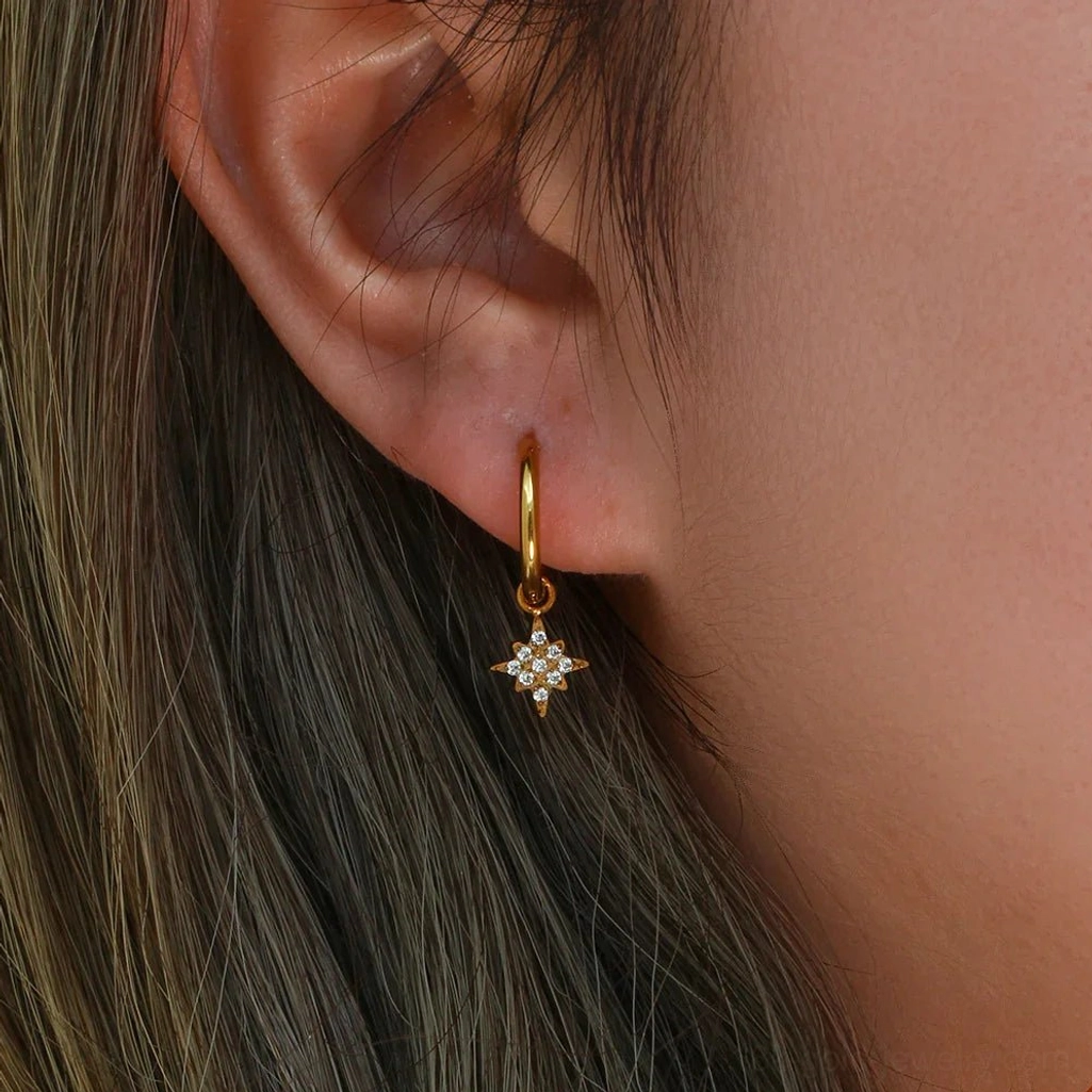 Woman wearing single 18K gold starburst drop huggie earring close-up side view on ear