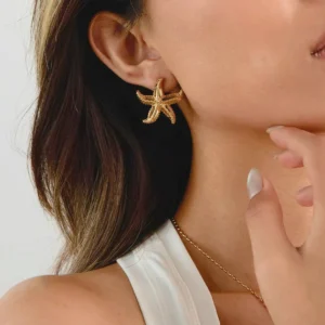 Gold starfish stud earrings worn on female model's left ear, close-up side view showing lightweight comfort and elegant fit