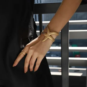 Gold starfish cuff bracelet worn on wrist with matching starfish ring on hand outdoor balcony setting black outfit