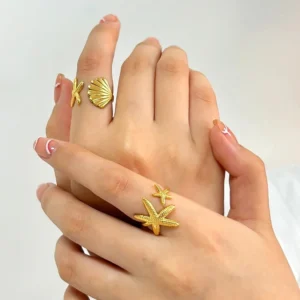 Woman wearing stackable 18K gold marine themed rings on multiple fingers close-up hand view with french manicure
