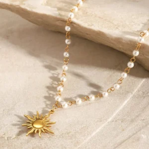 18K gold pearl necklace overhead view - sun pendant with pearl accents on textured beige stone surface from above