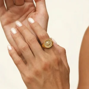 Close-up detail of 18K gold sunface ring worn on female model's index finger, showing intricate sun face carving and crystal detailing