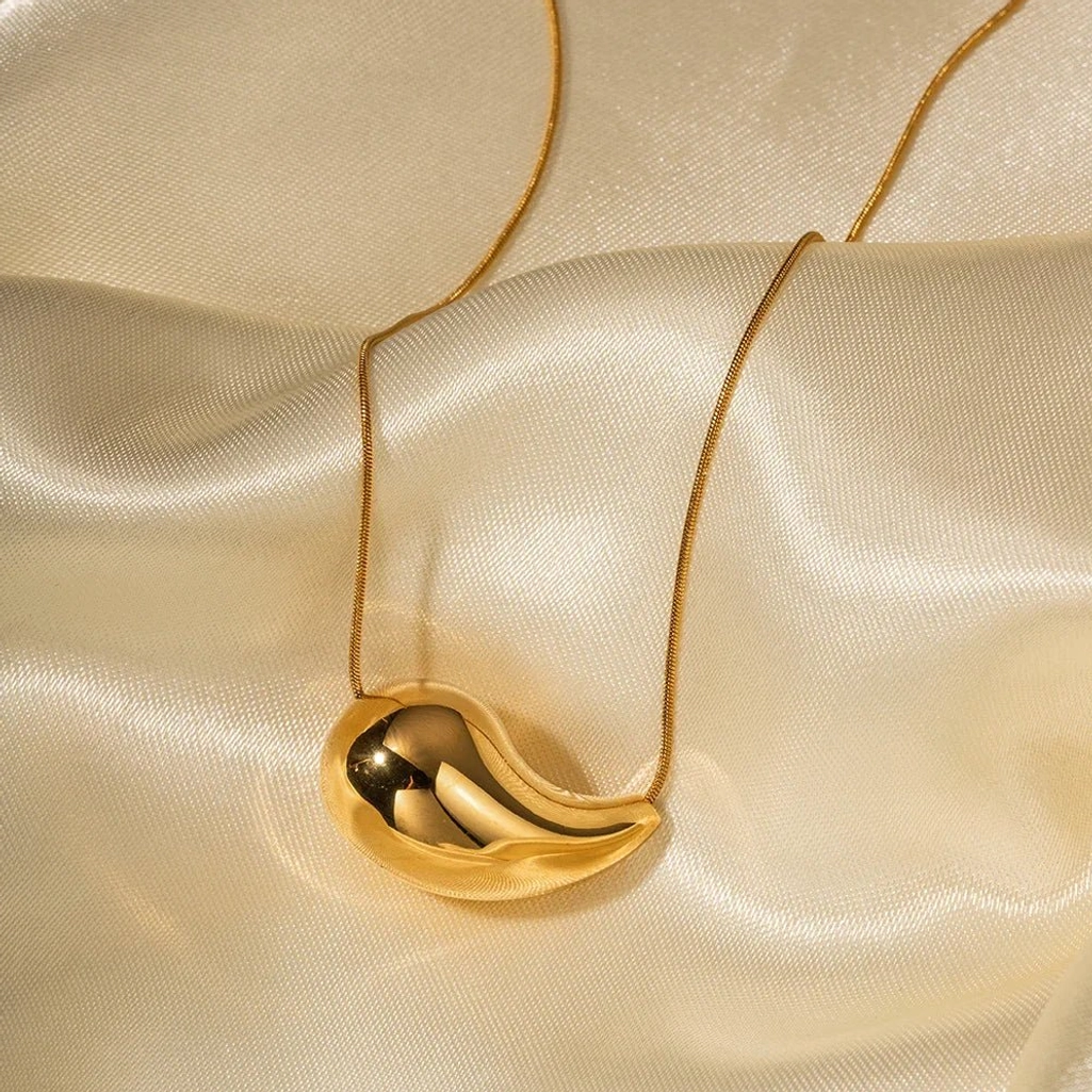 Gold teardrop pendant necklace on satin fabric - overhead flat lay product shot showing warm gold tone and reflective surface