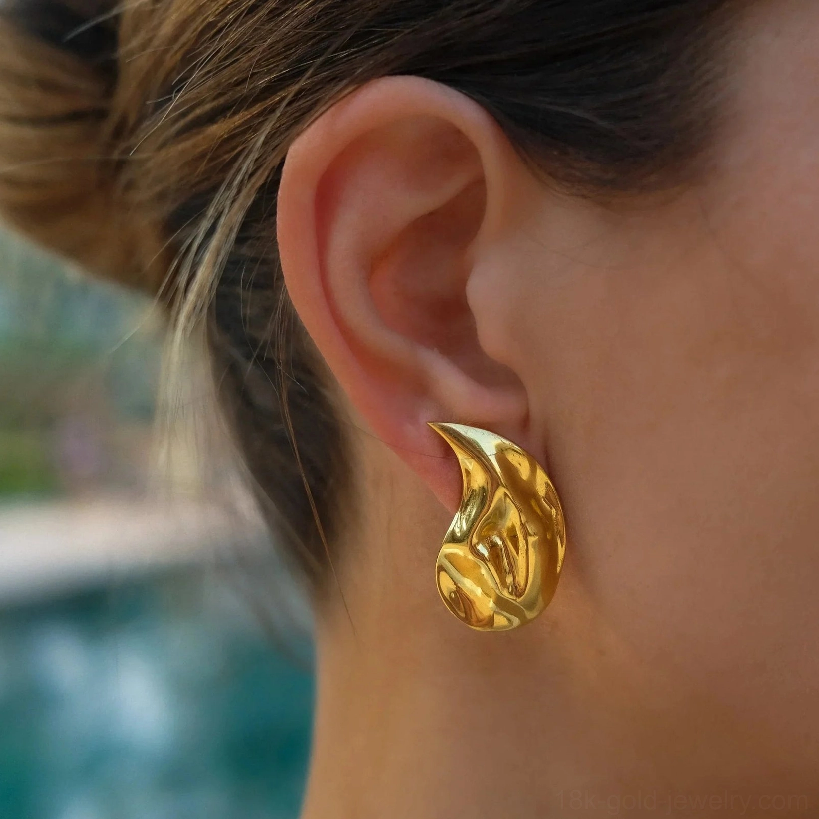 Gold teardrop earrings worn on female earlobe, close-up side view demonstrating fit, comfort and polished gold tone against skin