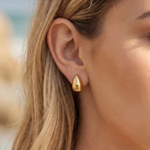 Single 18K gold teardrop huggie earring close-up side view on ear showing snug fit and sleek gold finish