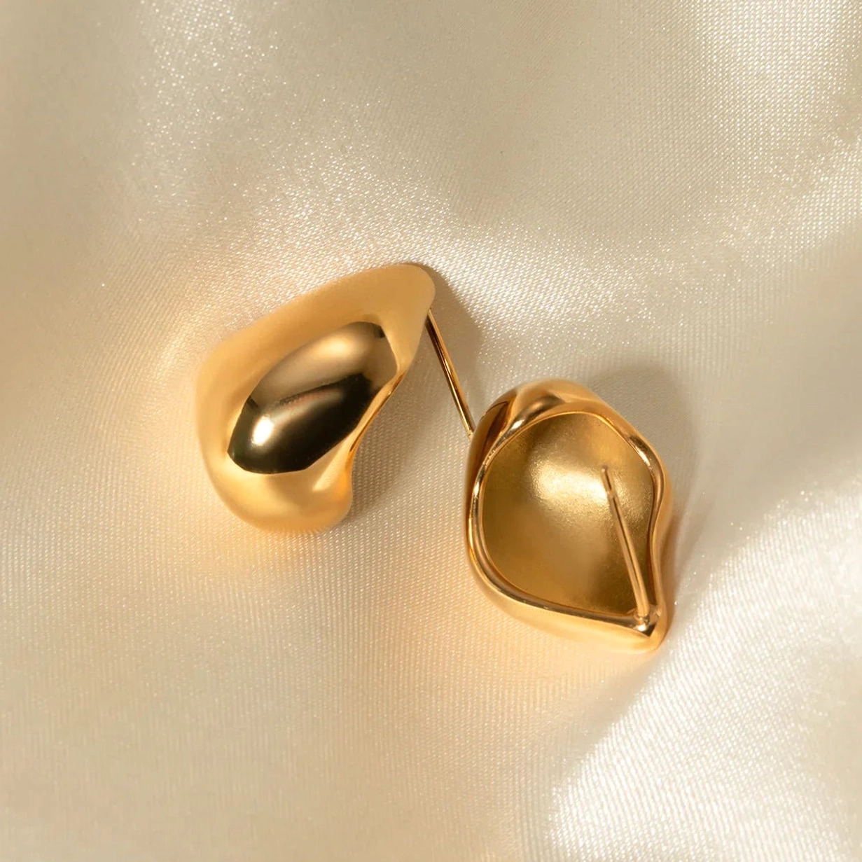 18K gold teardrop stud earrings satin fabric background high gloss polish