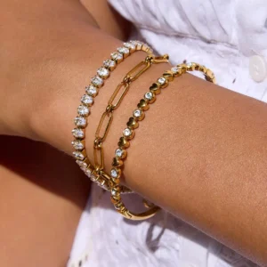 18K gold tennis bracelet stacked with chain bracelets worn on tanned skin, close-up inner forearm