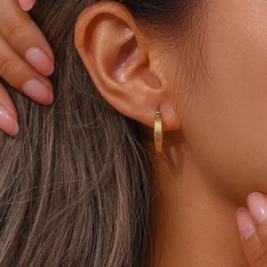 Model wearing 18K gold textured hoop earring on ear, demonstrating comfortable fit and elegant appearance on brown-haired woman