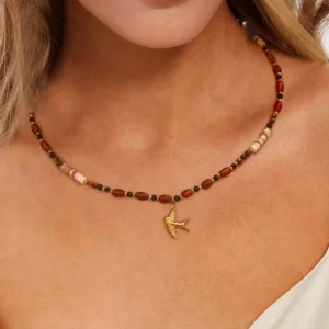 Tiger eye beaded necklace worn on model neck, close-up view showing natural stone beads resting on collarbone with gold swallow charm, bohemian style pendant jewelry