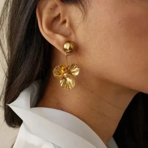 18K gold drop earrings worn on model side profile close-up view dangle design textured gold flower pendant with dark hair white blouse