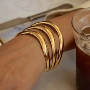 18K gold triple layer bangle worn on wrist close-up side view dining lifestyle setting with coffee