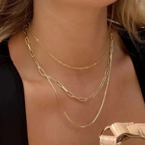 Woman wearing 18K gold triple-layer necklace on black top showcasing layered chain textures close-up neck view