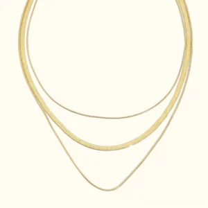 18K gold triple layered necklace flat lay - three-chain set with mixed widths and polished gold finish on neutral background