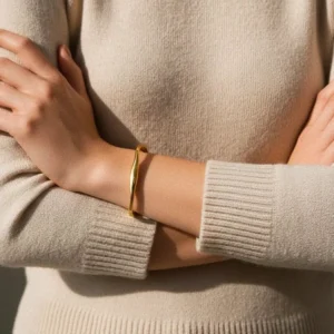 Woman wearing 18K gold twisted bangle on wrist - cream knit sweater close-up styling