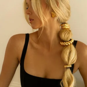 Woman wearing 18K gold twist ponytail cuff with matching gold drop earrings, blonde hair styled in elegant ponytail