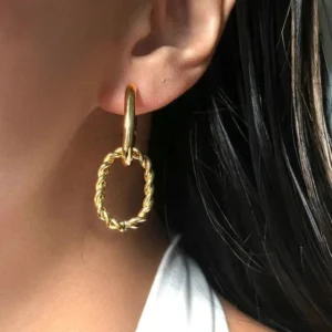 Close-up side view of 18K gold hoop earrings worn on ear, featuring smooth huggie hoop with twisted oval drop pendant, hypoallergenic stainless steel