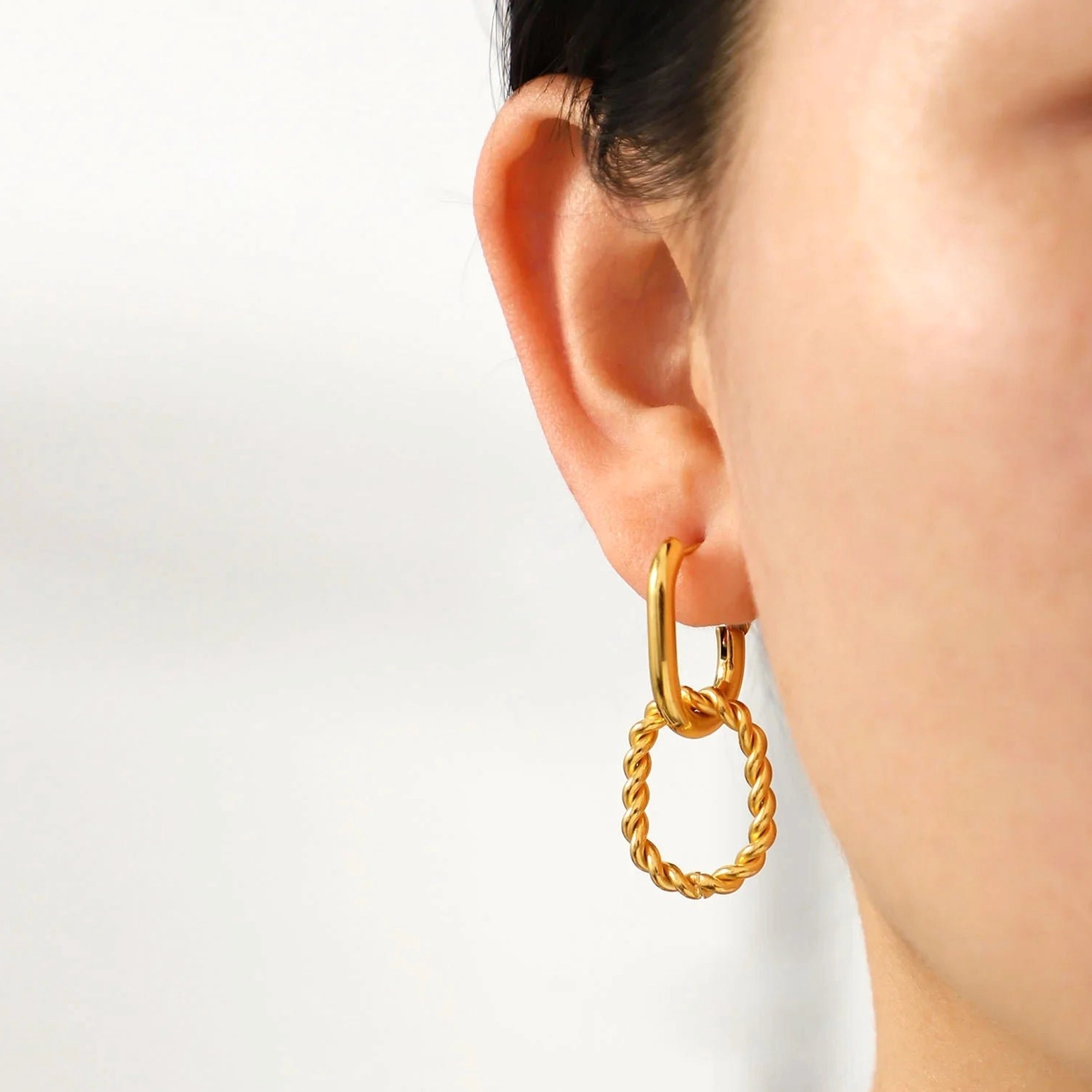 Front ear view of 18K gold twisted hoop earrings, displaying smooth huggie hoop with textured oval drop pendant, tarnish-free PVD coating