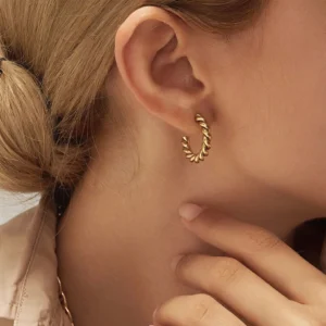 Gold twisted hoop earring on ear close-up side view worn by woman showing snug fit and rope design texture