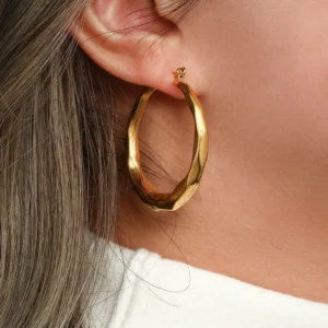 Gold twisted hoop earrings worn on model ear, close-up side view showing secure hinge closure and fit