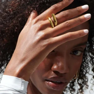 18K gold twisted knot ring worn on hand, close-up of woman wearing gold dual-bar ring with white manicure and white collared shirt