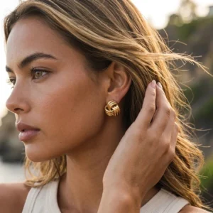Woman wearing 18K gold twisted knot earrings in side profile outdoors - natural lighting showing how earrings enhance profile and complement light complexion