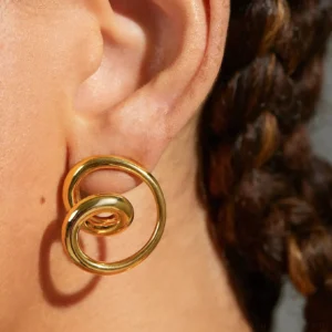 Gold spiral stud earrings worn on ear close-up side view on model with braided hair
