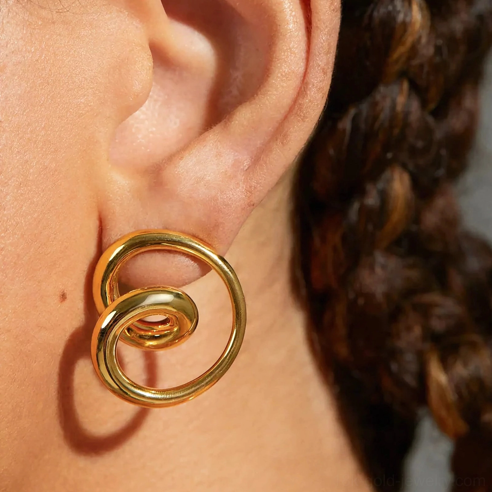 Gold spiral stud earrings worn on ear close-up side view on model with braided hair