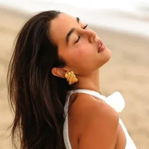 18k gold twisted wave stud earrings worn on model ear beach outdoor setting side profile close-up