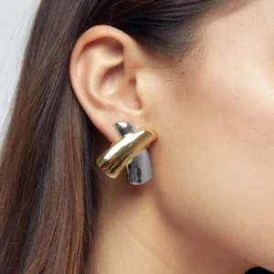 Two-tone gold and silver twisted X stud earrings worn on ear, close-up side view on female model, mixed metal dual tone smooth glossy finish