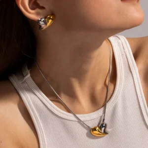 Model wearing two-tone 18K gold heart necklace and matching dual-tone stud earrings set with white ribbed tank top