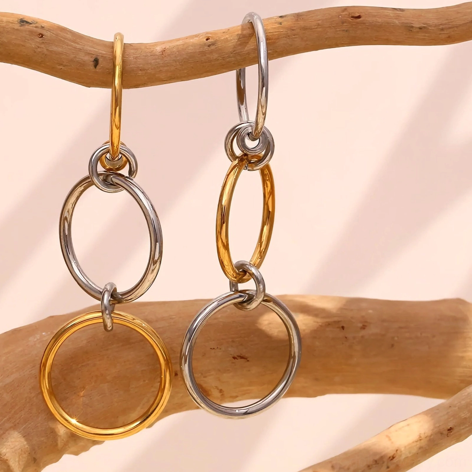 two-tone silver and gold interlocking drop hoop rings linked metal design flat lay on wooden branches neutral warm lighting